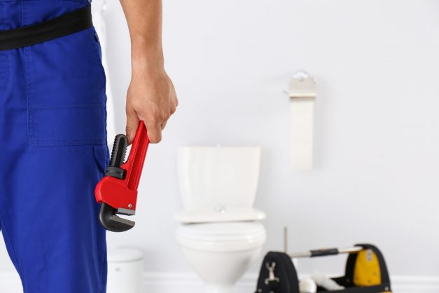 Young man with plumber wrench and toilet bowl on background