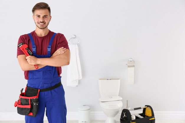 Young man with plumber wrench and toilet bowl on background